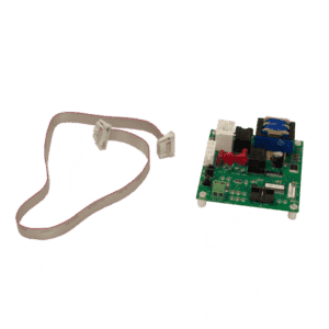 A green printed circuit board with various electronic components sits on white standoffs, next to a flat gray ribbon cable. This setup is ideal for integration with an automatic grease removal or self-cleaning grease trap system.